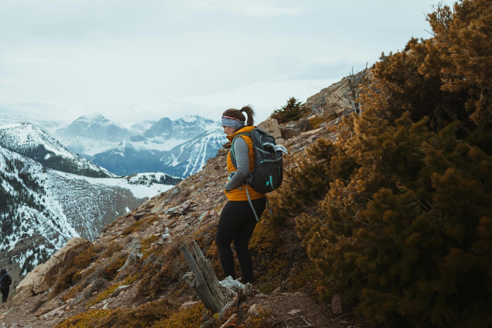 A woman in sportswear trekking through a scenic mountain landscape with snow-capped peaks.